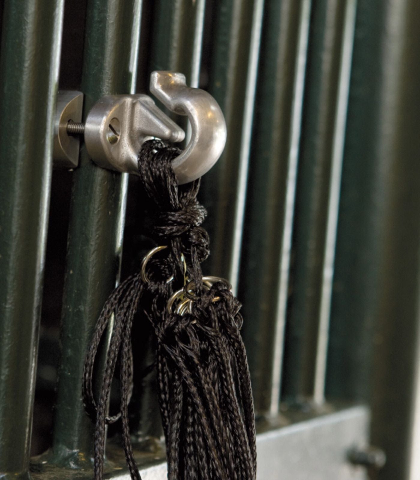 Silver hook holding the top of a haynet attached to the bars of a stable